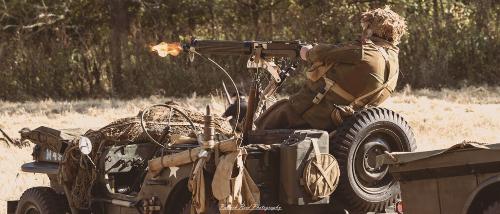 "Image of a military jeep equipped with a mounted machine gun, actively firing during a combat scenario. The scene captures the intensity of battle, with the gunner focused and determined as shells eject from the weapon. The jeep, adorned with camouflage patterns, moves across a rugged terrain, emphasizing its role in modern warfare. Smoke and debris from the firing enhance the chaotic atmosphere of the battlefield, highlighting the adrenaline and urgency of military operations."